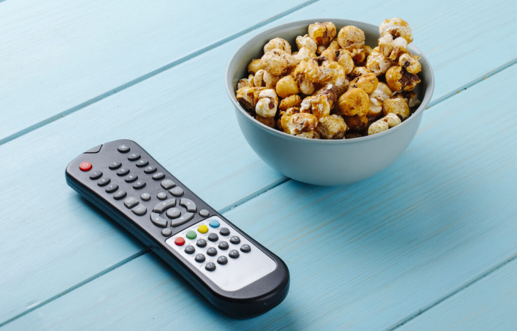 side view of sweet caramel popcorn in a bowl and tv remote on blue background