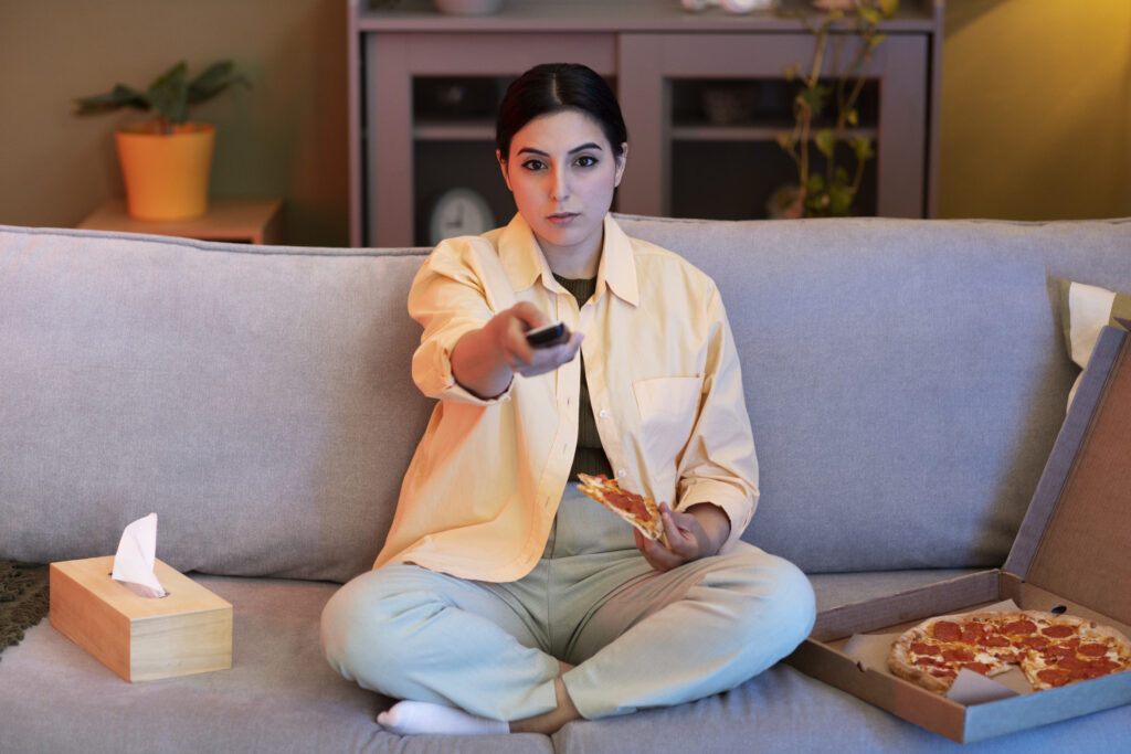 young woman eating pizza watching tv